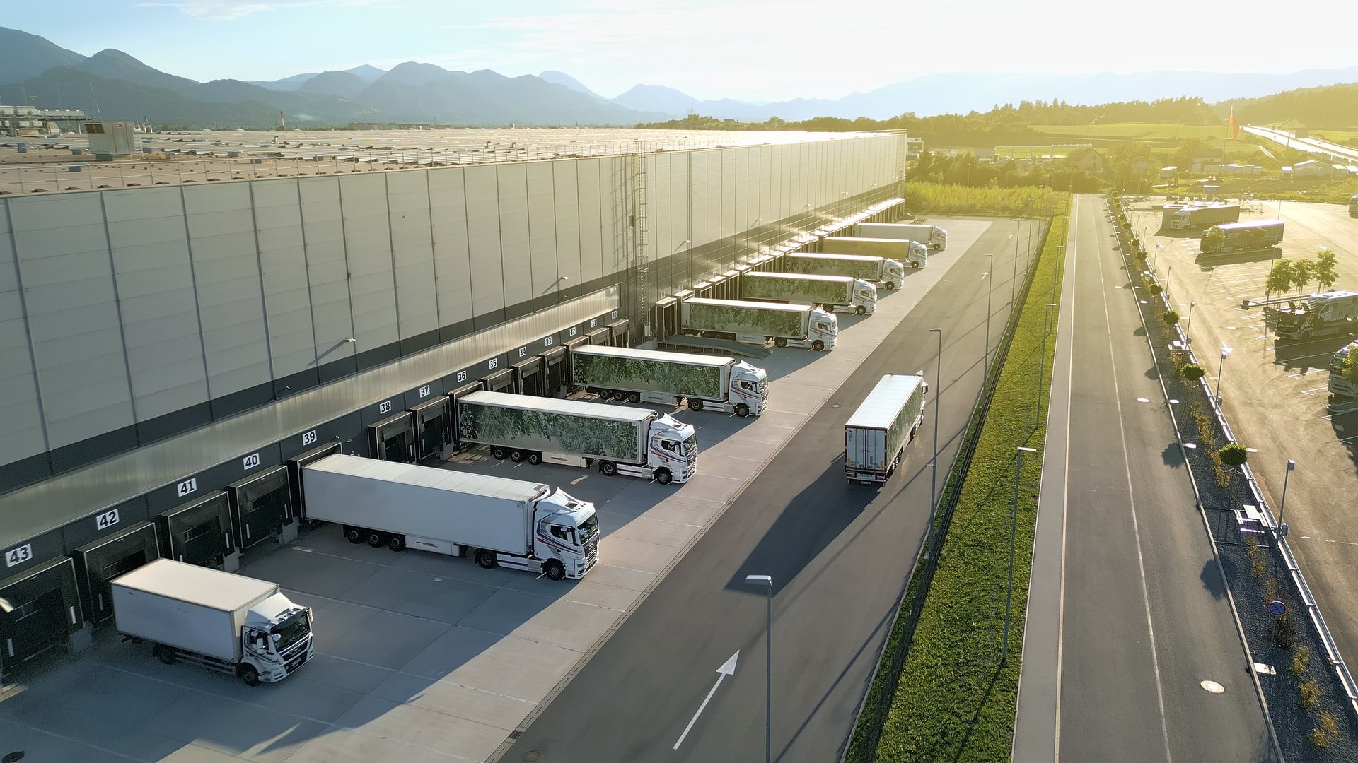 Aerial view of distribution warehouse with trucks at loading docks against mountain backdrop