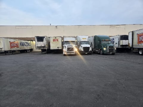 Row of commercial delivery trucks and trailers parked in front of a large warehouse building