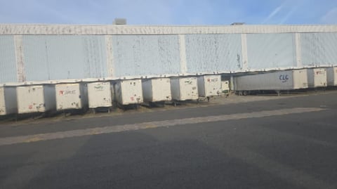 Row of white shipping containers lined against industrial corrugated metal building wall