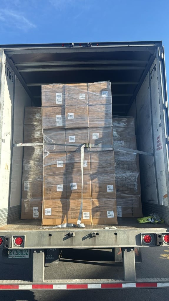 Open cargo truck bed filled with stacked and wrapped wooden pallets against blue sky