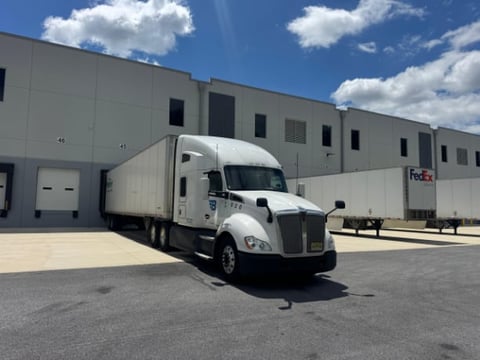 White semi truck with FedEx trailer parked at loading dock of industrial warehouse building under blue sky